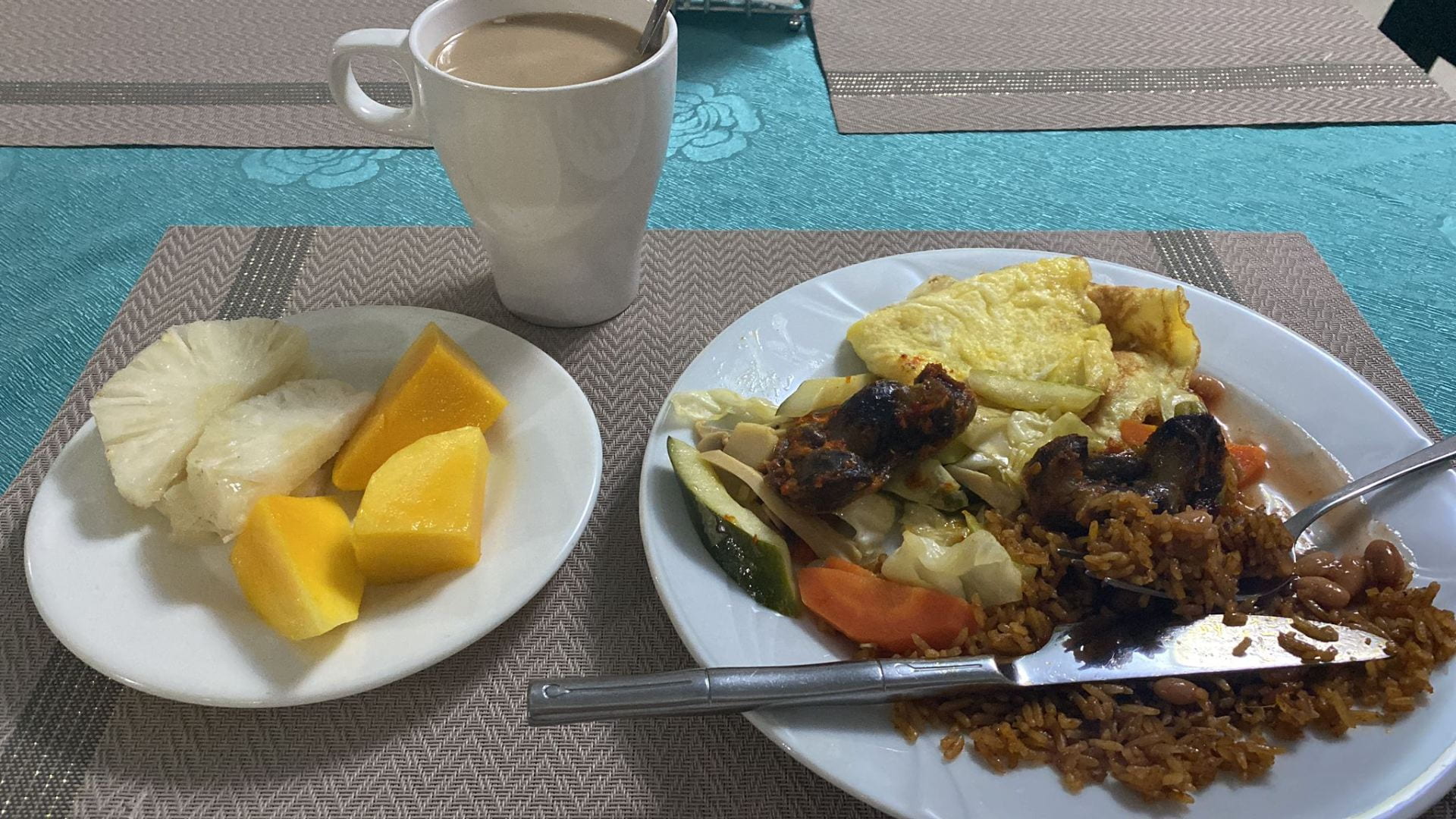 A breakfast plate containing rice, eggs, gizzards, vegetables, and fruit.